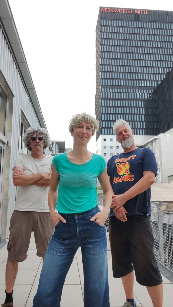Pat Peroni, Pauseline und Kurti stehen auf einer Steinterrasse im Werksviertel in München